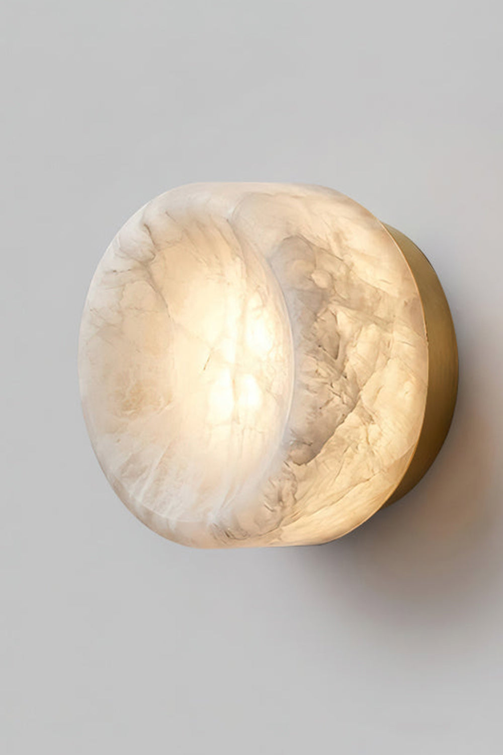 Isolde Concave Alabaster Disc Wall Sconce | Natural Alabaster and Black Metal | Studio close-up shot of the lit sconce featuring a matte black finish base on a light wall | vexa lamps