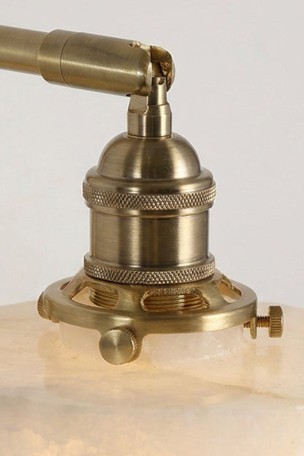 Liora Scalloped Alabaster Wall Sconce | Natural Alabaster and Brushed Brass | Extreme close-up preview of the polished brass hardware socket and top screw connections on the stone shade | vexa lamps