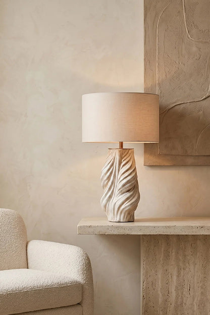 Adara Sculptural Ceramic Table Lamp | Ceramic, Fabric | Displayed on a modern floating travertine ledge next to a cream armchair against a minimalist textured plaster wall nook | vexa lamps