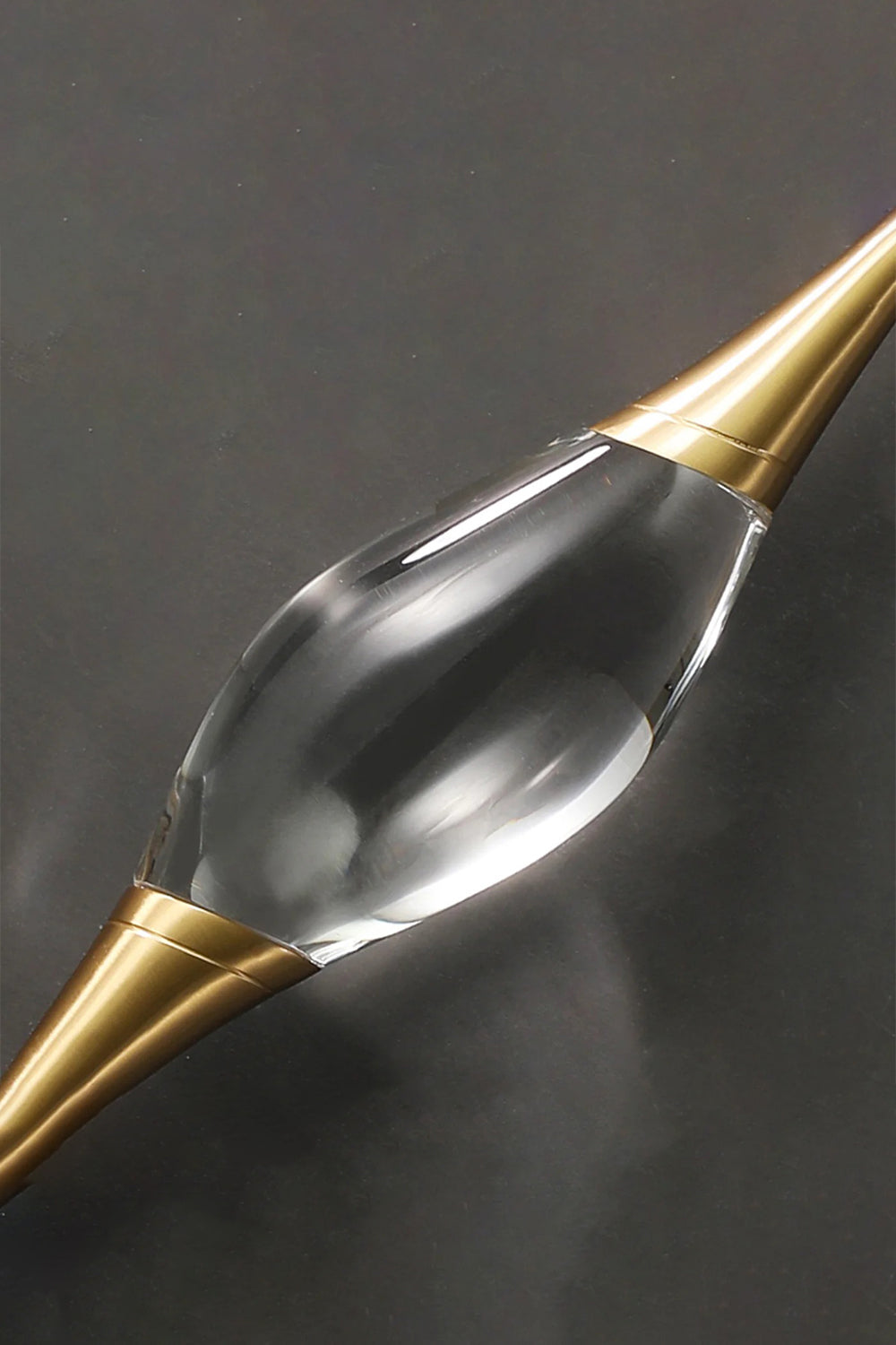 Astraea Crystal Linear Wall Sconce | Crystal, Brass | Macro close-up detail of the clear sculpted crystal core and the sleek gold brass conical holder on a dark background | Detail shot | vexa lamps