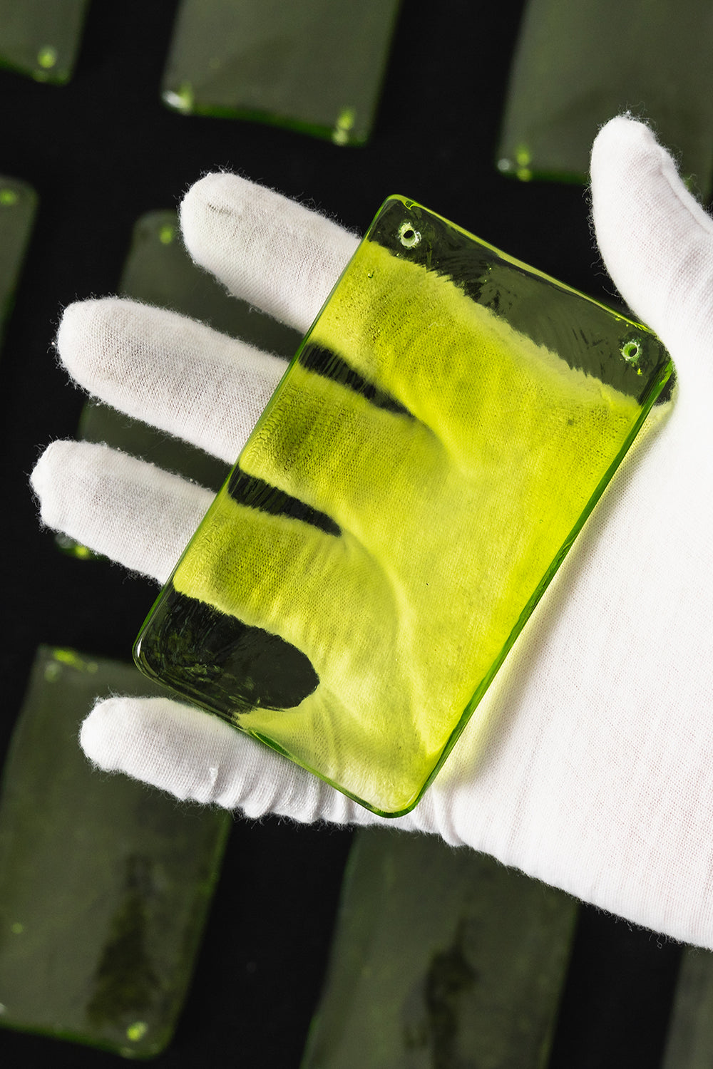 Aura Verdant Tiered Green Glass Ceiling Light | Metal, Glass | A white-gloved hand holding a single translucent textured green glass plate to show its color and transparency | Detail shot | vexa lamps