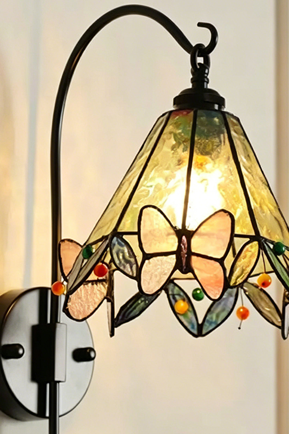 Aura Vine Stained Glass Wall Sconce | Glass, Metal | Close-up side profile of the illuminated wall lamp showing the curved black arm, mount base, and glowing glass panels | Detail shot | vexa lamps