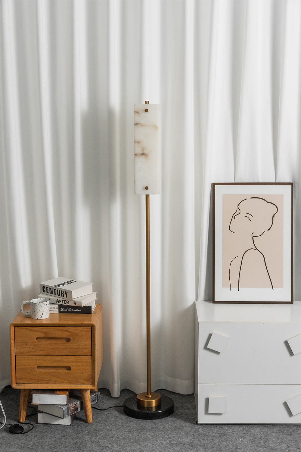 Aurelius Alabaster Brass Floor Lamp | Alabaster, Brass | Studio staged unlit view of the minimalist linear standing lamp set between a wooden nightstand and white drawers against a vertical pleated backdrop | vexa lamps
