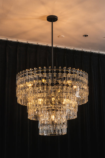 Aven Tiered Glass Prism Chandelier | Glass, Metal | Full view of the illuminated tiered crystal fixture casting a soft golden glow against a dramatic dark wall backdrop | vexa lamps
