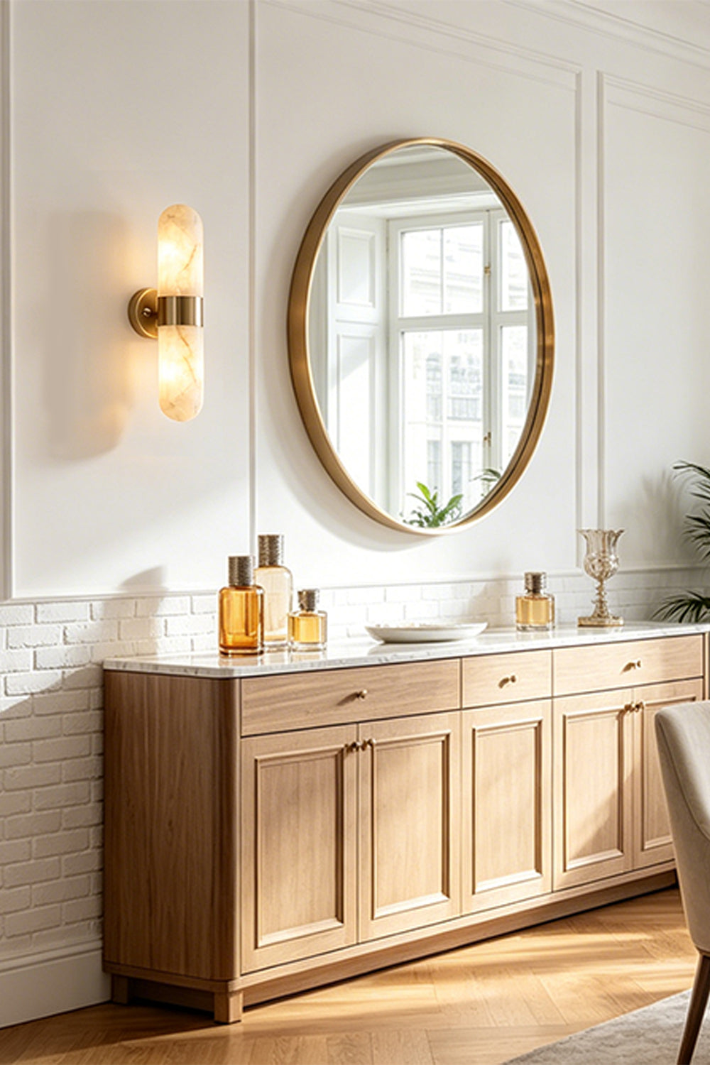 Calla Alabaster Capsule Wall Sconce | Alabaster, Brass | Mounted elegantly on a white wall next to a large round gold mirror and a wooden sideboard cabinet in a luxury hallway | vexa lamps