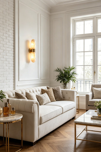 Calla Alabaster Capsule Wall Sconce | Alabaster, Brass | Providing a warm ambient glow on a white paneled wall in a sophisticated living room next to a cream fabric sofa | vexa lamps