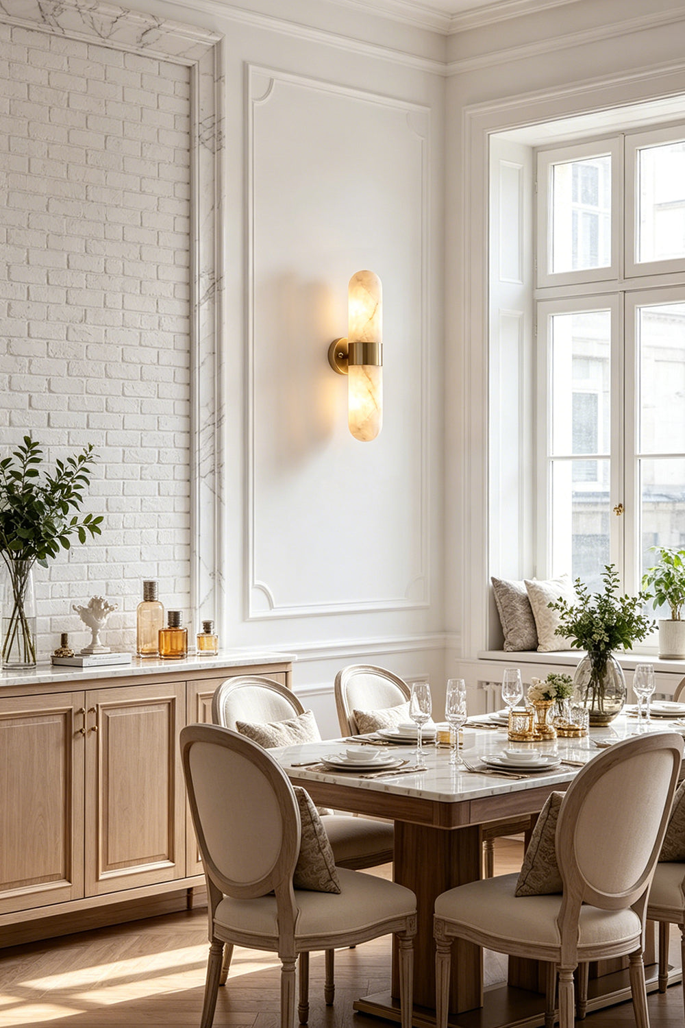 Calla Alabaster Capsule Wall Sconce | Alabaster, Brass | Installed in a refined classical dining room casting a soft light near a wooden dining table and upholstered chairs | vexa lamps