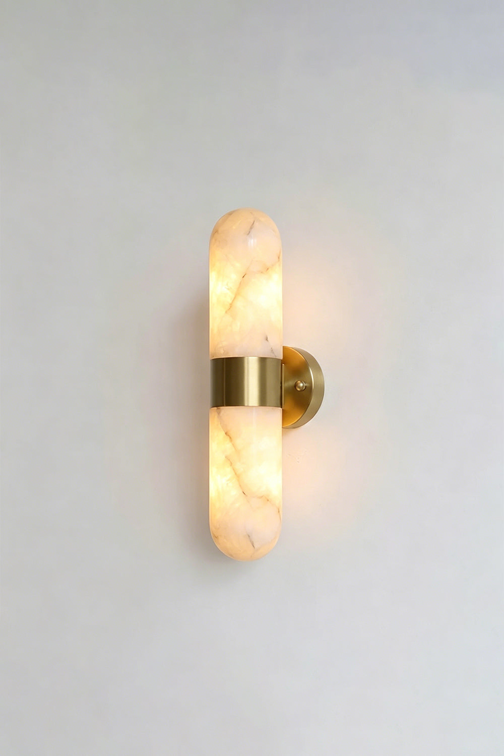 Calla Alabaster Capsule Wall Sconce | Alabaster, Brass | Alternative lit studio view of the brushed brass stone sconce radiating a soft warm white glow | vexa lamps