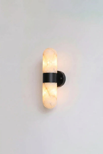 Calla Alabaster Capsule Wall Sconce | Alabaster, Metal | Studio front view of the fully lit matte black hardware variant casting a warm yellow halo against a plain background | vexa lamps