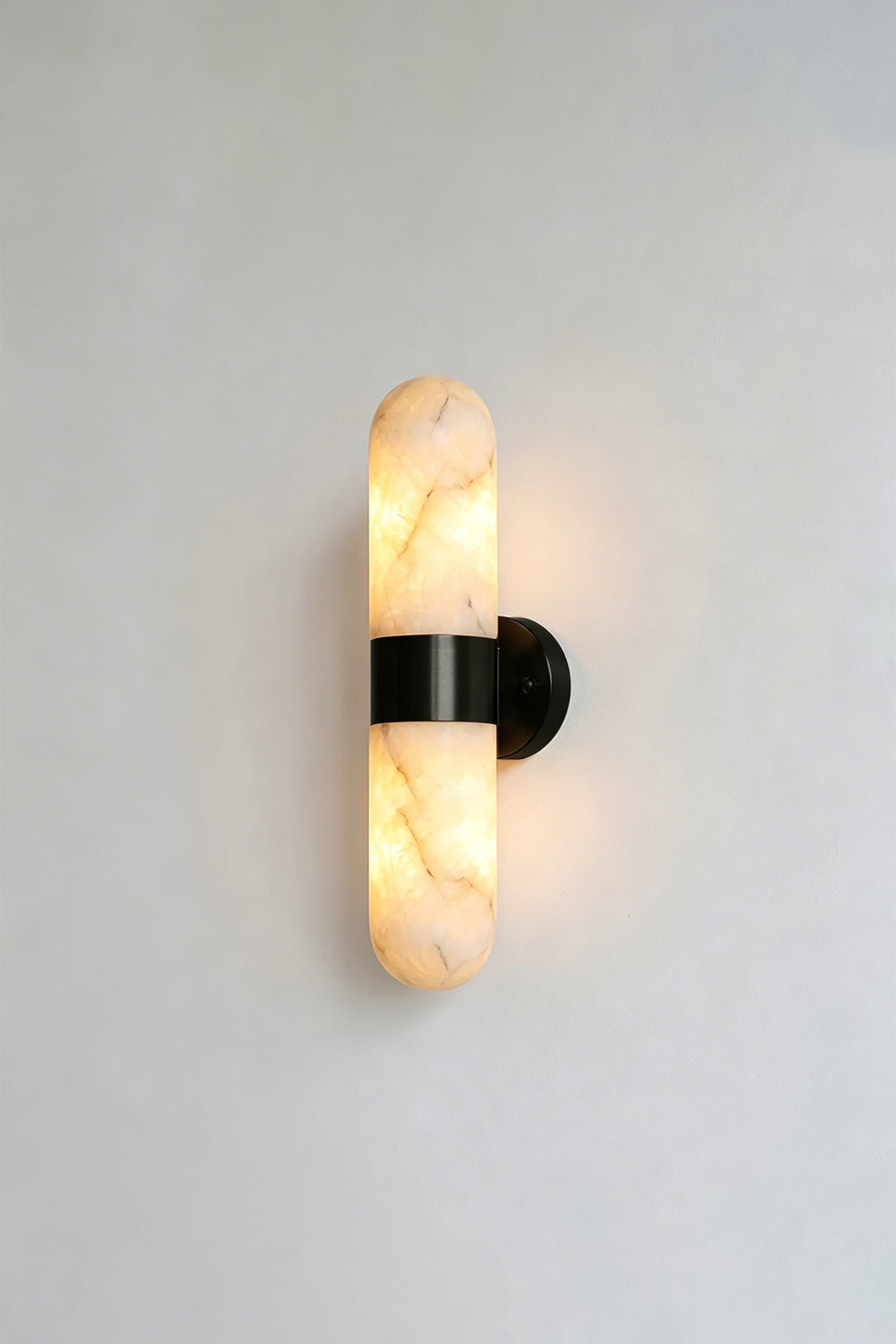 Calla Alabaster Capsule Wall Sconce | Alabaster, Metal | Lit studio view of the industrial modern matte black hardware finish variant against a white studio background | vexa lamps