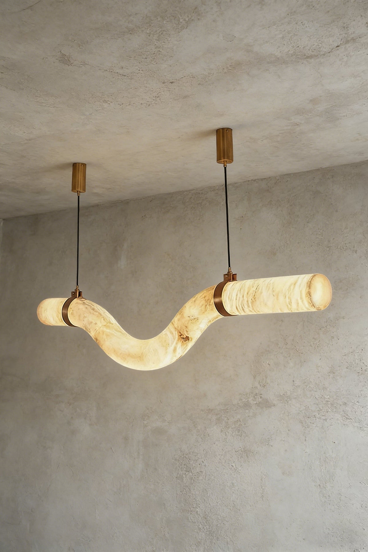 Lit undulating alabaster tube chandelier against grey ceiling | Alabaster, Brass | Side perspective showing the organic shape | vexa lamps