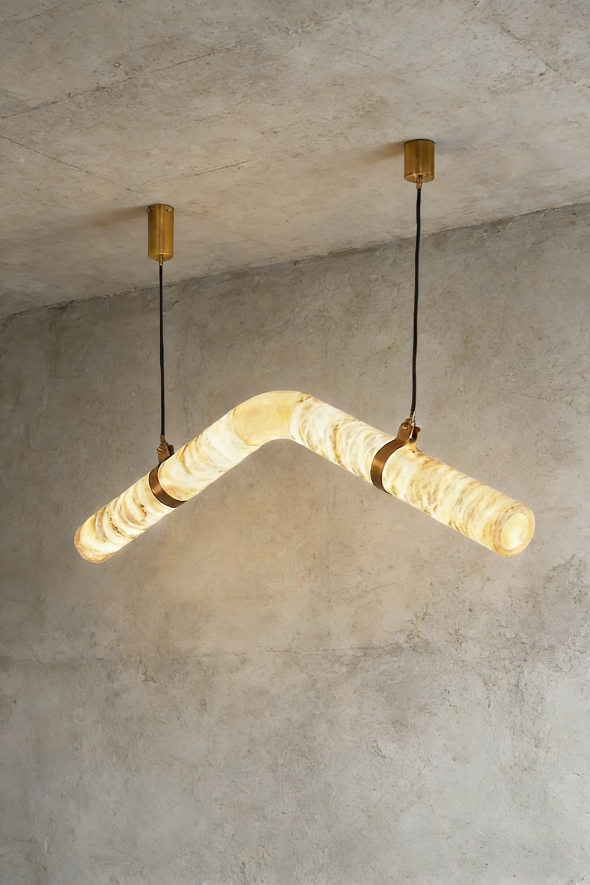 Lit undulating alabaster tube chandelier against grey ceiling | Alabaster, Brass | Side perspective showing the organic shape | vexa lamps