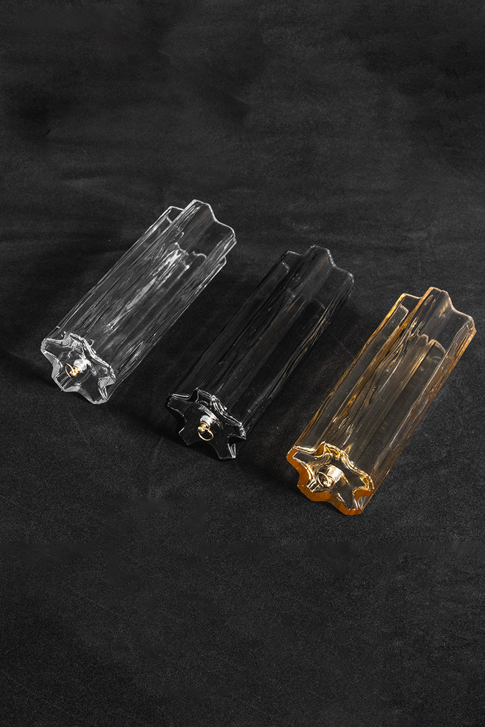 Elysian Tiered Fluted Ceiling Light | Glass, Metal | Close-up focus on three variant options of fluted glass prism rods (clear, smoky, and amber) resting on a black background | Detail shot | vexa lamps