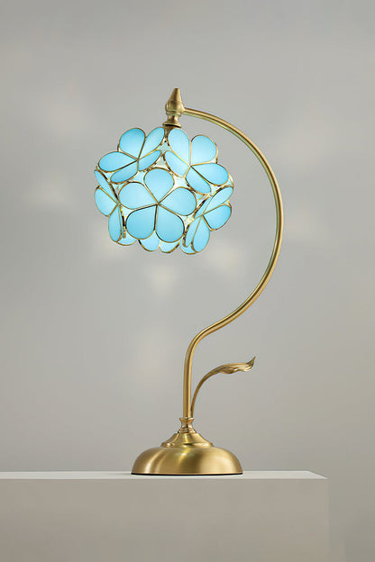 Evanthe Blossom Stained Glass Table Lamp | Stained Glass, Metal | Studio front view of the vibrant sky blue variant fully illuminated on a white pedestal block against a grey wall | vexa lamps