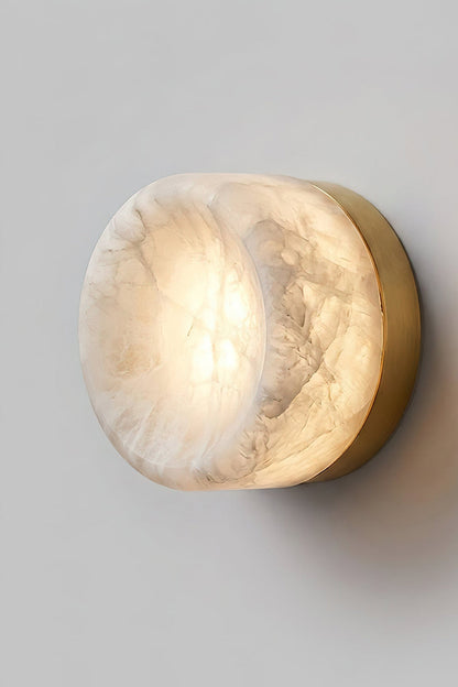 Isolde Concave Alabaster Disc Wall Sconce | Natural Alabaster and Black Metal | Studio close-up shot of the lit sconce featuring a matte black finish base on a light wall | vexa lamps