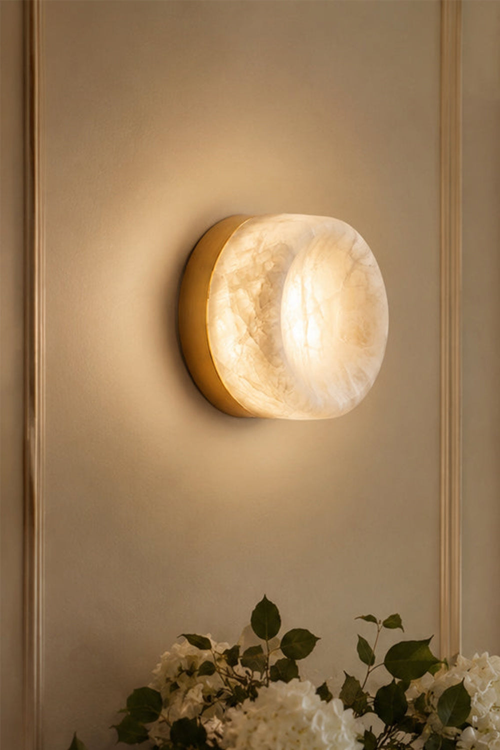 Isolde Concave Alabaster Disc Wall Sconce | Natural Alabaster and Brass | Close-up of the fixture glowing on a beige wall creating a beautiful light halo | vexa lamps