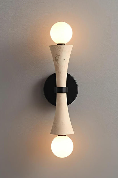 Katia Travertine Hourglass Wall Lamp | Travertine, Metal | Studio front view of the fully illuminated hourglass stone wall fixture casting a brilliant dual-directional warm light halo against a grey backdrop | vexa lamps