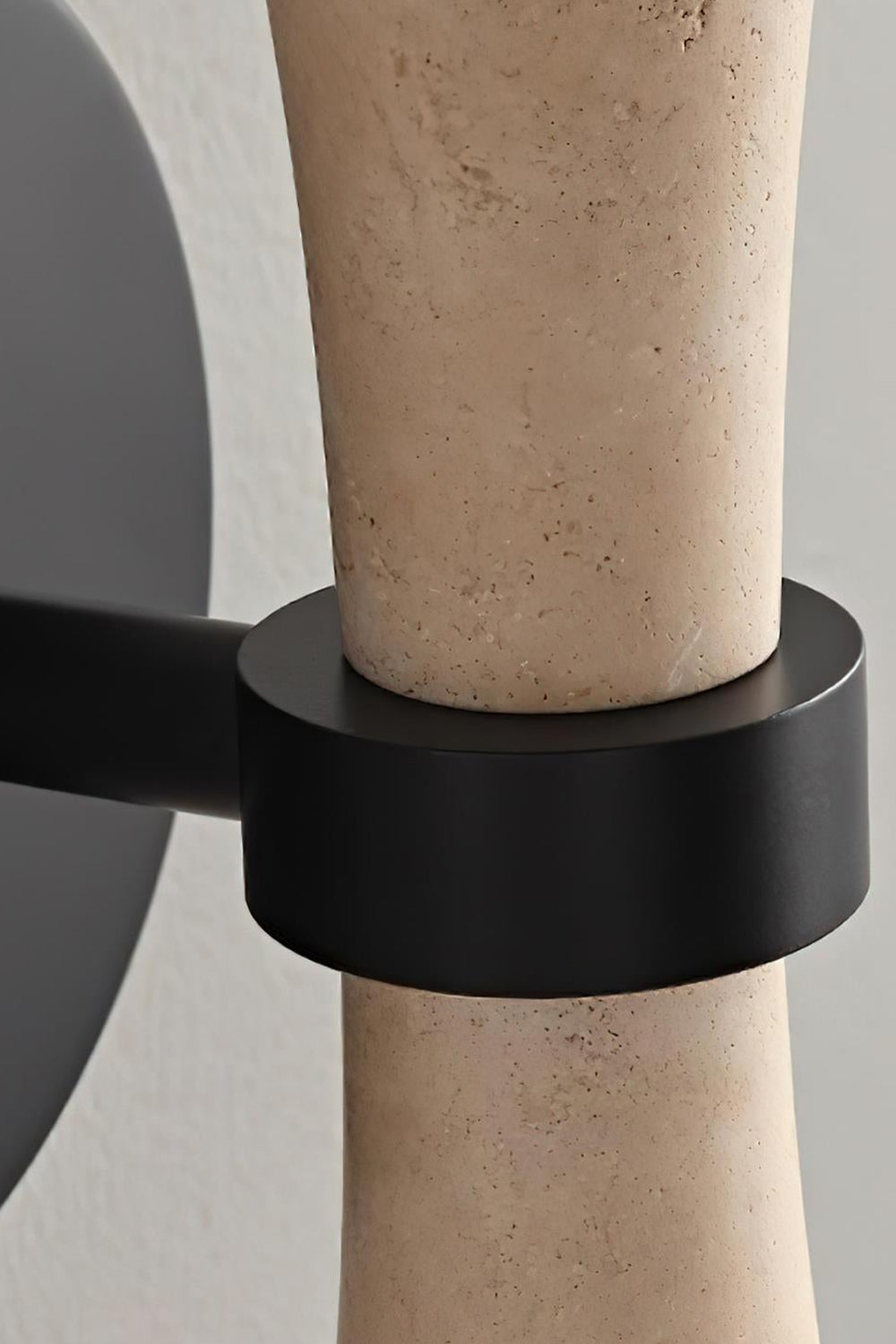 Katia Travertine Hourglass Wall Lamp | Travertine, Metal | Macro close-up focusing on the seamless connection of the matte black metallic wall base mount and holding ring structure | Detail shot | vexa lamps
