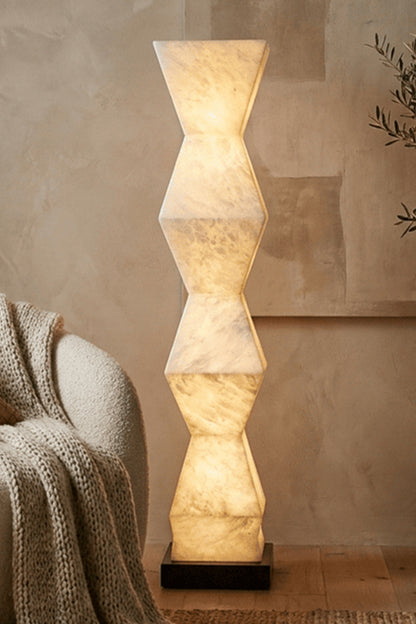 Kellan Geometric Alabaster Floor Lamp | Alabaster, Metal | Close-up shot of the illuminated natural alabaster stone lamp column glowing softly against an earthy textured wall background | vexa lamps