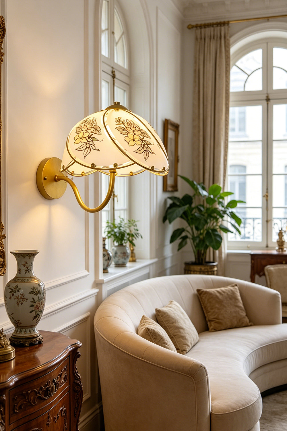 Lillian Retro Floral Wall Lamp | Glass, Metal | Providing a warm ambient glow over a curved cream sofa and antique wooden cabinet near a window | vexa lamps