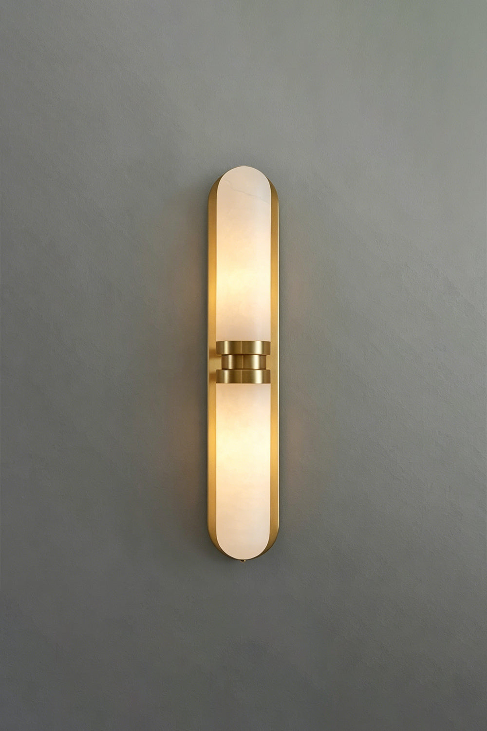 Linea Alabaster Capsule Wall Sconce | Alabaster, Brass | Frontal studio view of the fully lit linear capsule stone sconce casting a warm glow against a minimalist grey background | vexa lamps