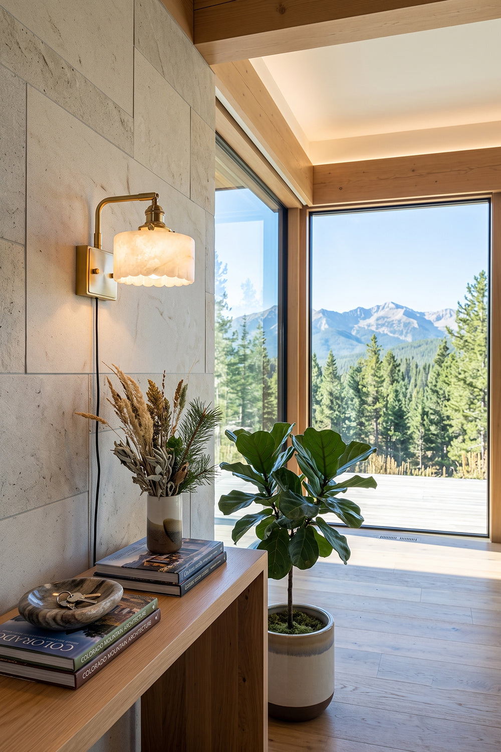 Liora Scalloped Alabaster Wall Sconce | Natural Alabaster and Brushed Brass | Styled in a modern hallway above a wooden console table near a large window with scenic mountain views | vexa lamps