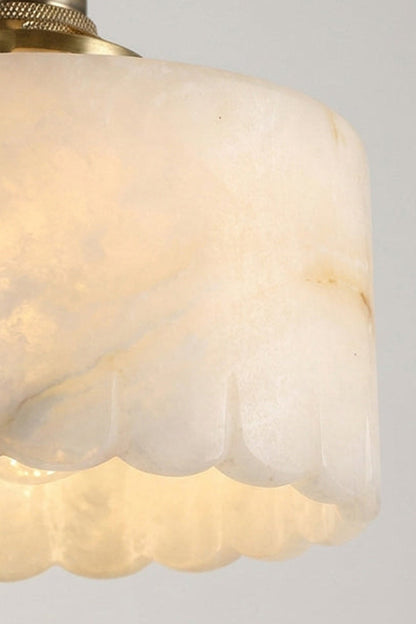Liora Scalloped Alabaster Wall Sconce | Natural Alabaster and Brushed Brass | Macro close-up shot focusing on the intricate wavy scalloped bottom edge of the lit translucent stone shade | vexa lamps