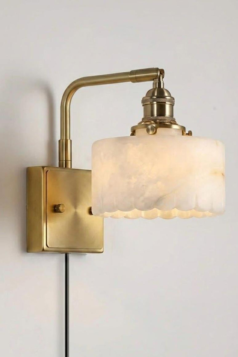 Liora Scalloped Alabaster Wall Sconce | Natural Alabaster and Brushed Brass | Standard studio single product view hanging fully lit with a plug-in cord against a light grey background | vexa lamps