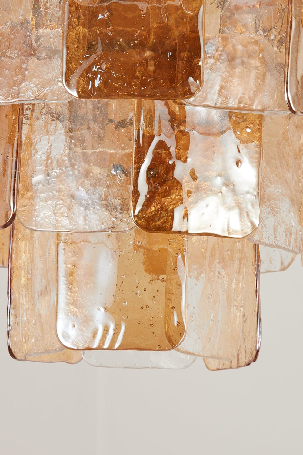 Lucia Tiered Amber Glass Chandelier | Glass, Metal | Close-up focus on the illuminated textured amber glass panels highlighting the crinkled ice-like surface and warm light transmission | Detail shot | vexa lamps