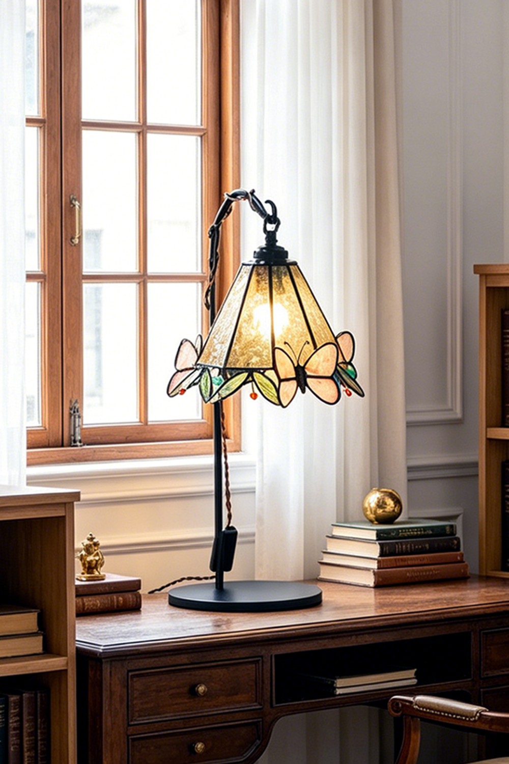Mariposa Stained Glass Table Lamp | Glass, Metal | Placed on a vintage dark wood desk in front of a bright arched window in a cozy study | vexa lamps