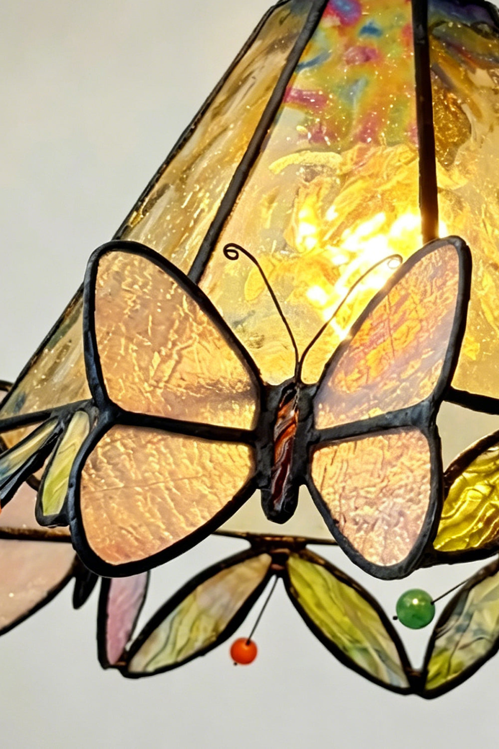 Mariposa Canopy Stained Glass Pendant Lamp | Glass, Metal | Macro focus on the illuminated yellow glass pattern, a butterfly, and colorful small glass gems along the rim | Detail shot | vexa lamps