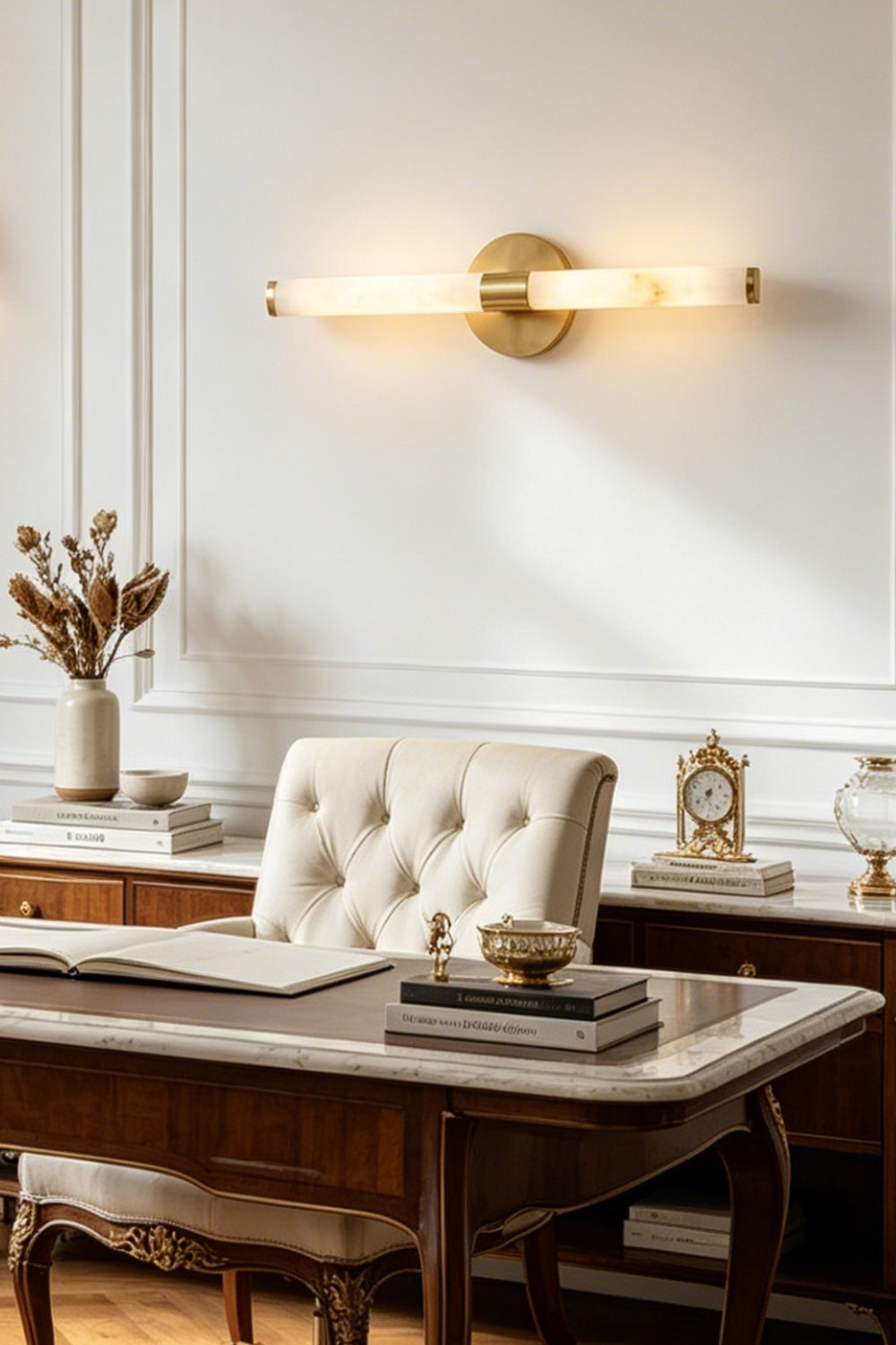 Nerida Linear Alabaster Wall Sconce | Alabaster, Brass | Staged interior view of the fully lit linear stone light fixture casting a warm halo over a traditional desk and a tufted leather chair | vexa lamps