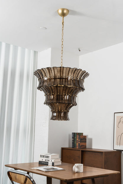 Octavia Sculptural Smoked Glass Chandelier | Dining Room Chandelier | Studio staged view of the fully illuminated tall multi-tiered glass fixture casting a warm golden glow near a table | vexa lamps