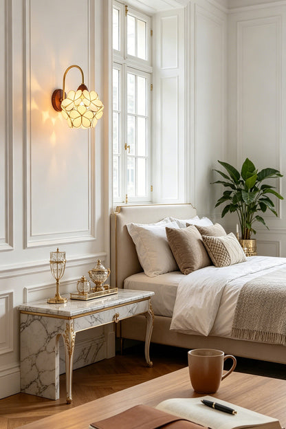 Rosalind Petal Glass Botanical Wall Lamp | Glass, Metal, Wood | Installed as a charming bedside reading light on a white paneled wall next to a bed with neutral linens | vexa lamps
