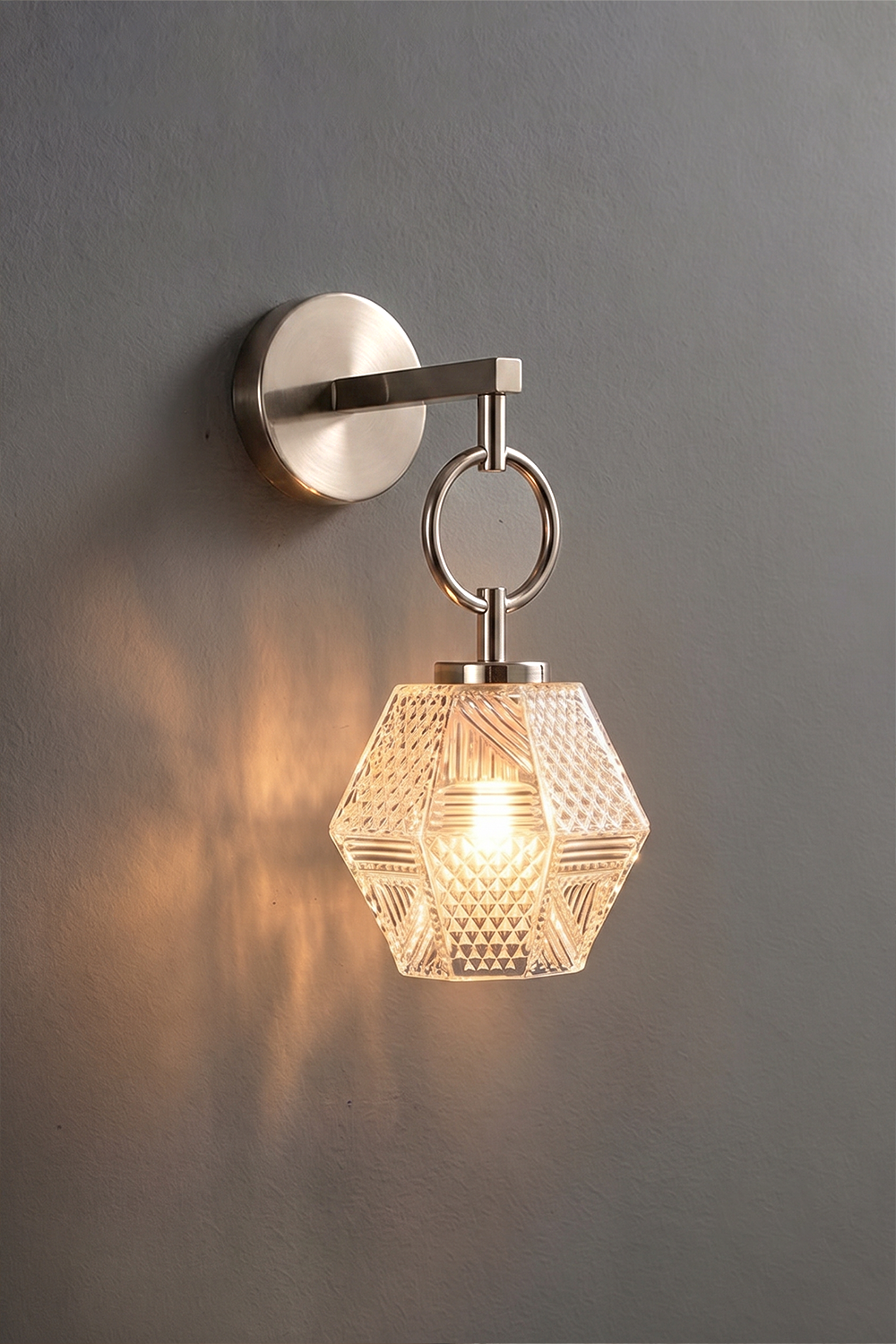 Rosamund Faceted Glass Wall Sconce | Faceted Glass and Silver Metal | Brushed nickel finish version glowing against a dark background | vexa lamps