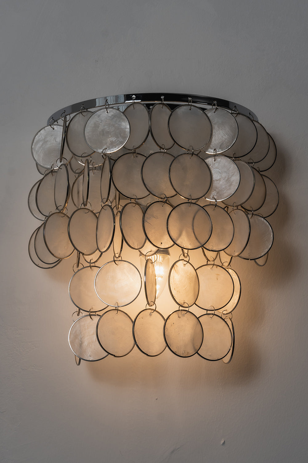 Front view of lit Capiz wall sconce | Shell | Iron | Product shot against a neutral studio background | vexa lamps