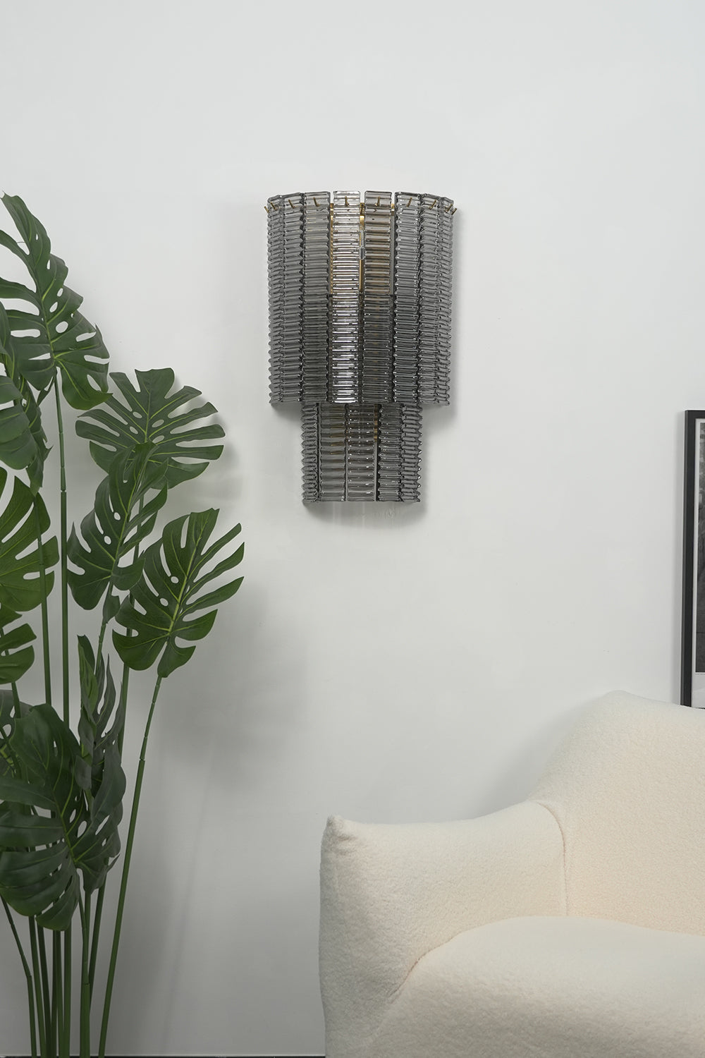 Sovereign Lattice Smoky Glass Wall Lamp illuminating a modern living space with a decorative plant.