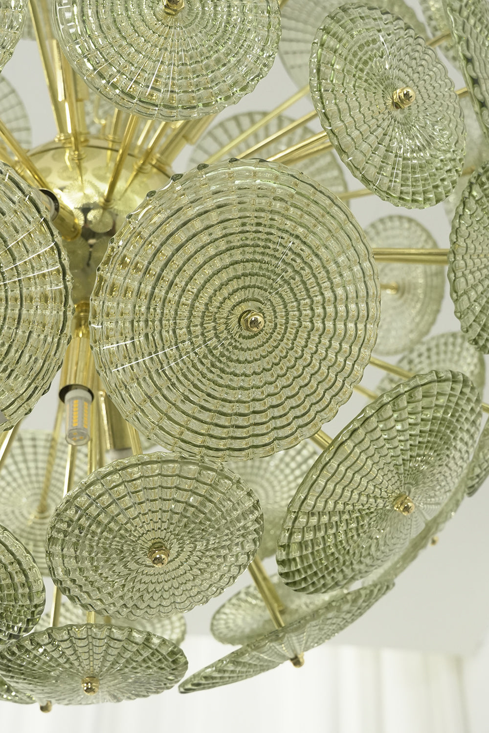 Detailed close-up of unlit green glass sunburst discs | Metal, Glass | Showing texture and brass attachment hooks | morylighting