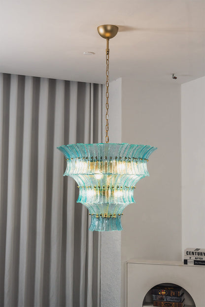 Thalassa Aquamarine Textured Glass Chandelier | Glass, Metal | Alternative studio shot of the illuminated tiered architectural glass light fixture hanging elegantly next to a grey drapery panel | vexa lamps
