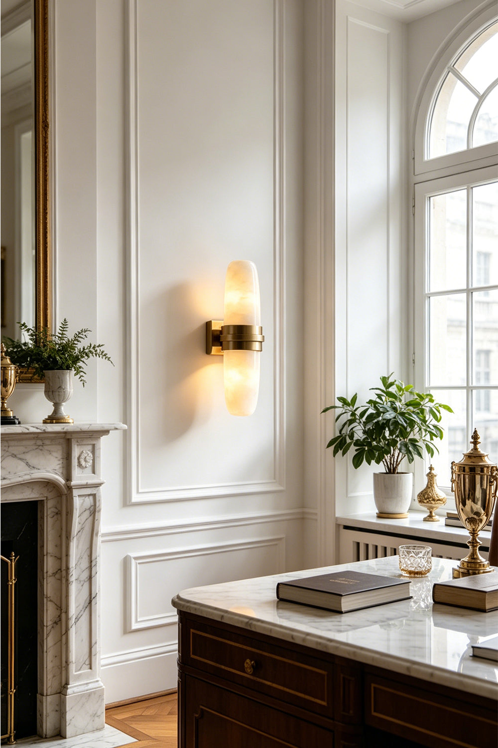 Theron Linear Alabaster Wall Lamp | Alabaster, Metal | Wall sconce casting a warm ambient glow near a classical white fireplace mantel and large bright windows | vexa lamps