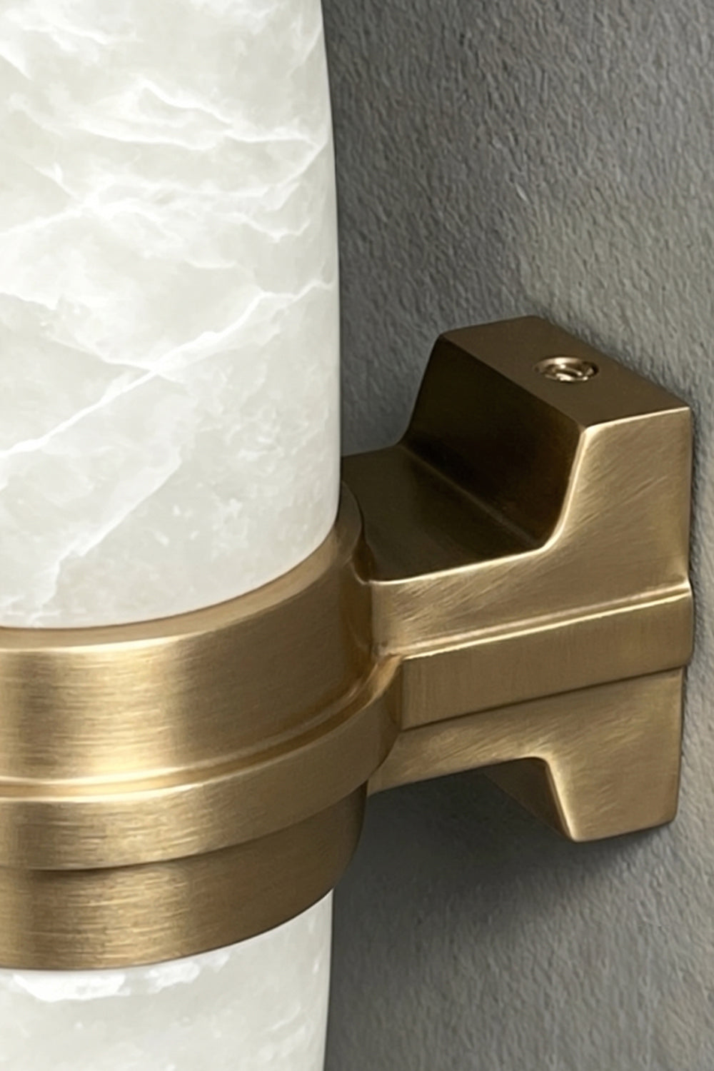 Theron Linear Alabaster Wall Lamp | Alabaster, Metal | Macro close-up view highlighting the brushed gold brass finish of the central support bracket against the natural stone veining | Detail shot | vexa lamps