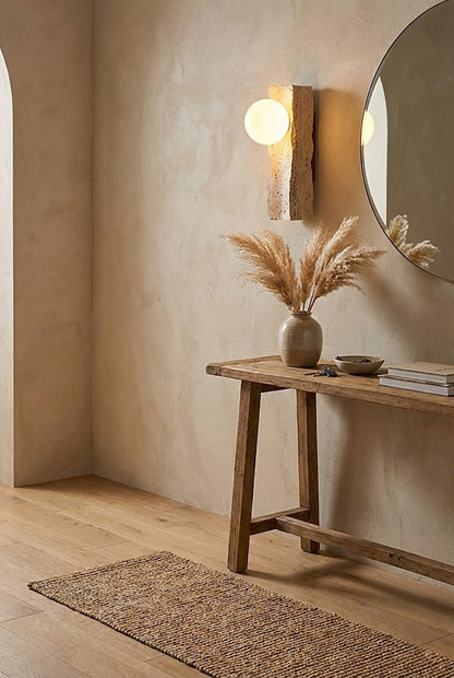 Travertine wall sconce in a hallway over console table | Yellow Travertine, Metal, Glass | Positioned next to a round mirror and dried flowers | vexa lamps