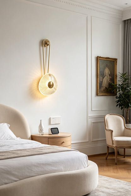Vara Aura Woven Acrylic Wall Lamp | Woven Acrylic, Brass | Installed as an elegant bedside reading sconce on a white wall next to a bed with neutral linens | vexa lamps